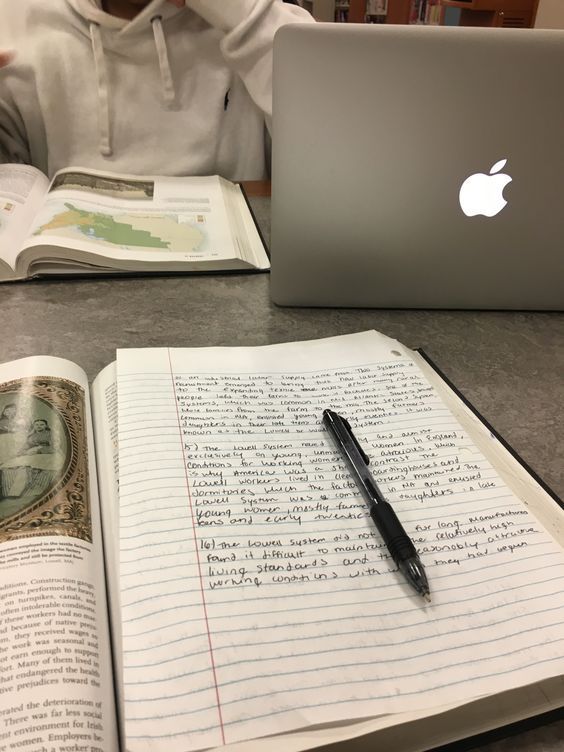 an open book with writing on it next to a laptop computer and a person sitting at a table