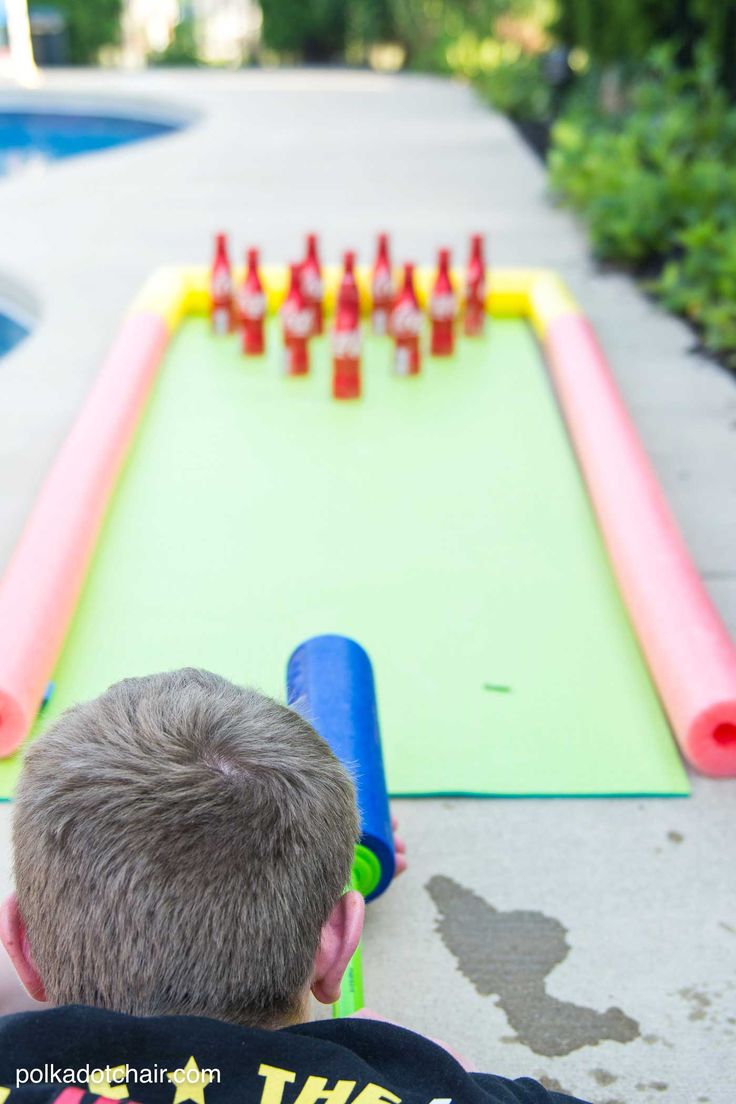 a young boy is playing with an inflatable bowling game on the sidewalk next to a swimming pool