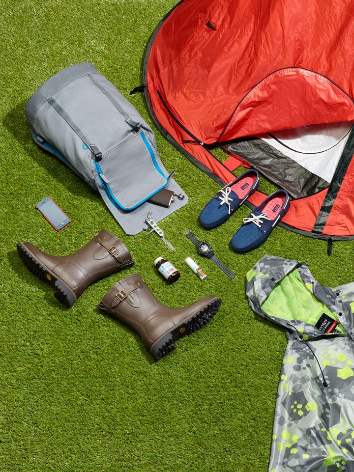 the contents of a camping kit are laid out on the grass, including an orange tent and rain boots