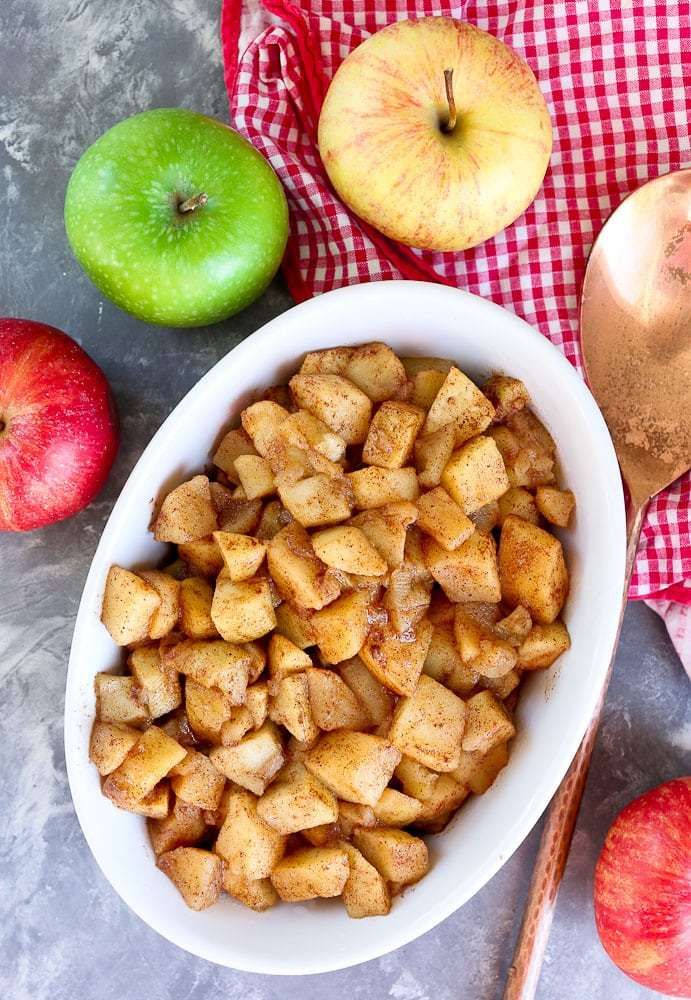 apples and cinnamon in a bowl next to spoons on a checkered table cloth