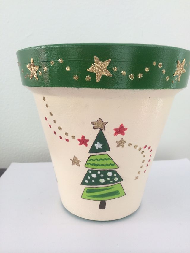 a green and white planter with a christmas tree painted on the side, sitting on a table