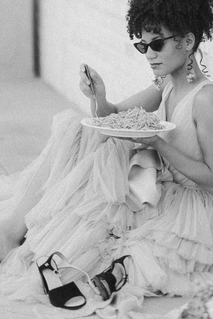 a woman sitting on the ground with a plate of food in her hand and wearing sunglasses