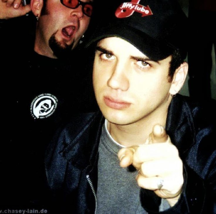 a man pointing at the camera with another man in the background behind him wearing glasses and a baseball cap