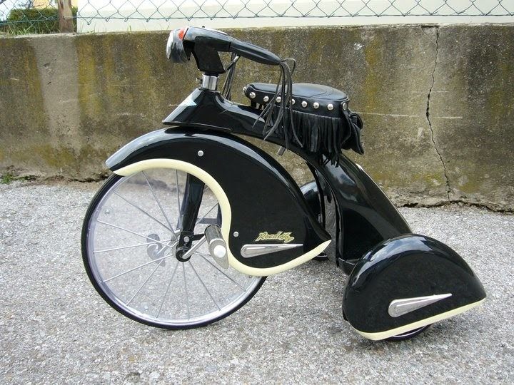 an old fashioned black and white motorcycle parked on the side of a road next to a cement wall