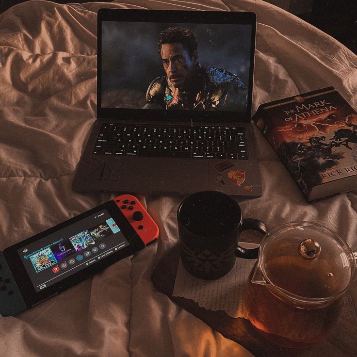 an open laptop computer sitting on top of a bed next to a nintendo wii game controller