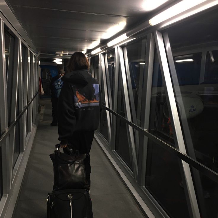 a person with a suitcase walking down a walkway next to some glass windows at night