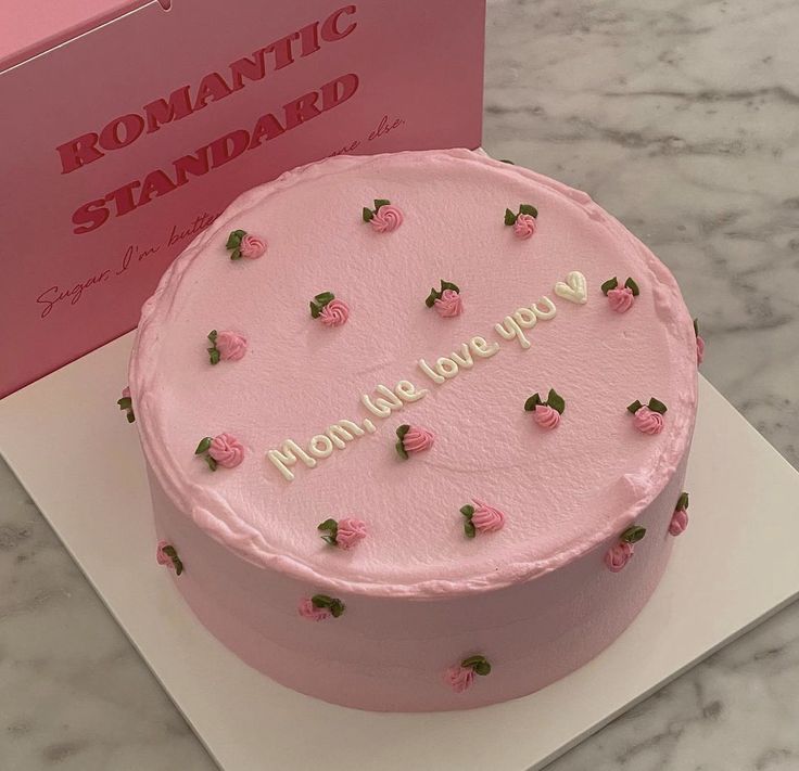 a pink cake sitting on top of a white plate next to a box with the word mom's love you written on it