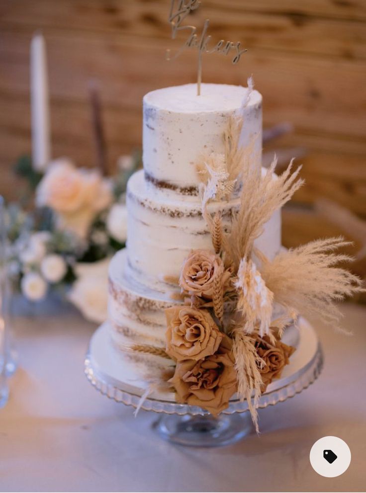 a three tiered wedding cake with flowers and feathers on the table next to candles