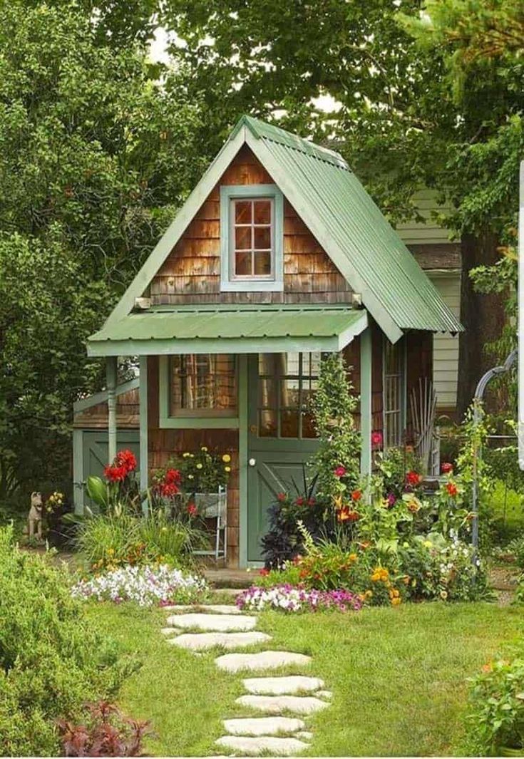 a small green house surrounded by trees and flowers