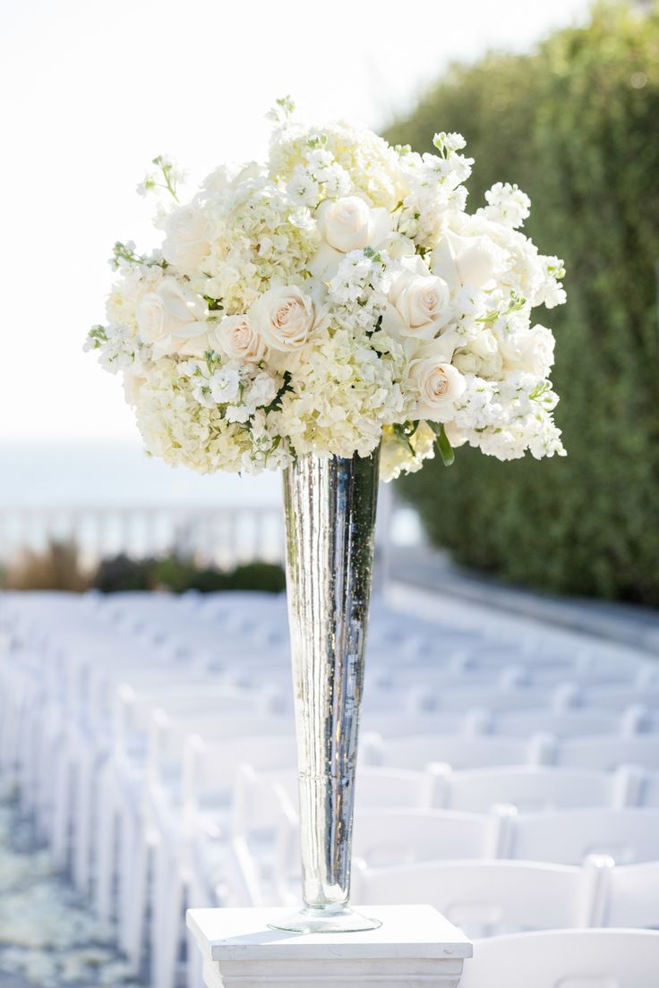 a vase filled with white and pink flowers on top of a table covered in chairs