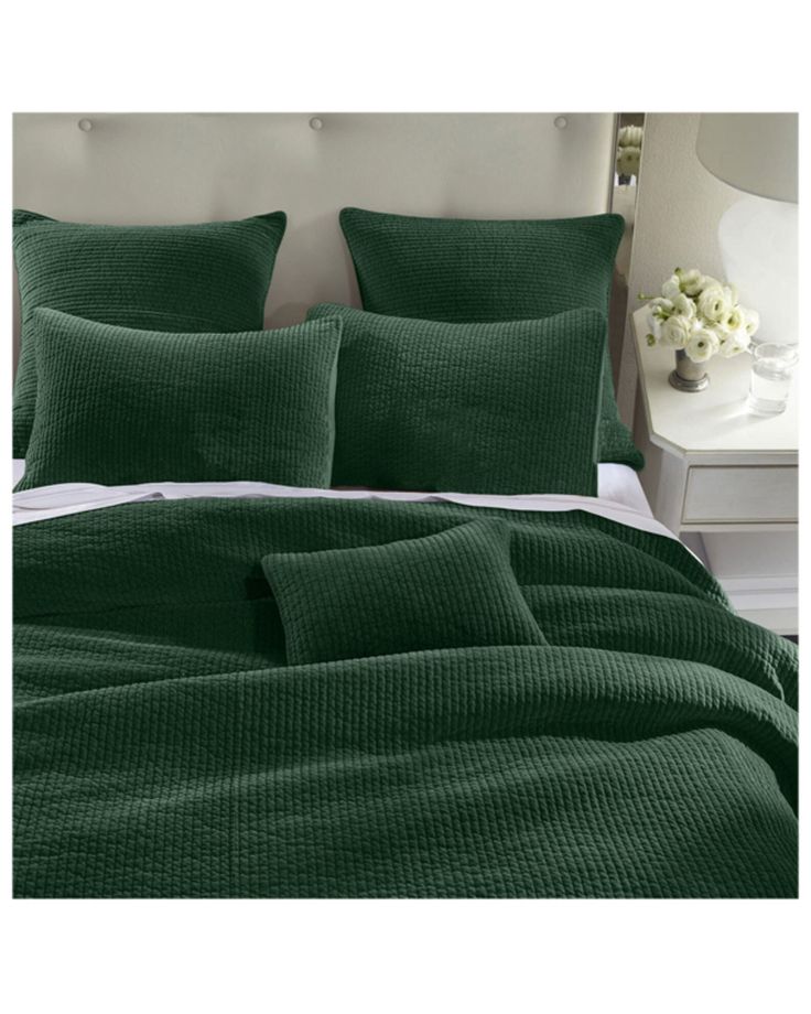 a bed with green sheets and pillows on top of it, next to a night stand