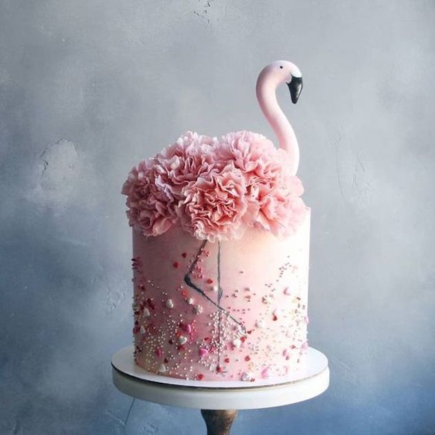 a pink cake decorated with flowers and a flamingo on top is sitting on a pedestal