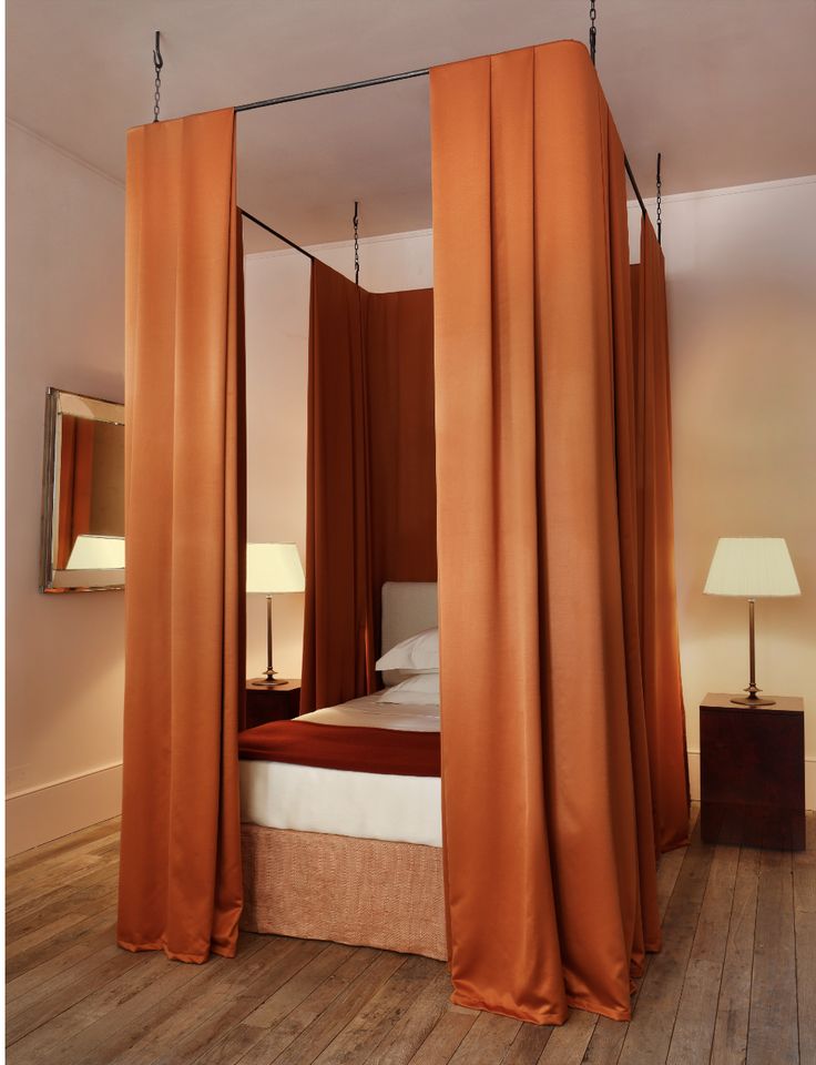 a bed with orange drapes hanging from it's sides and a mirror on the wall