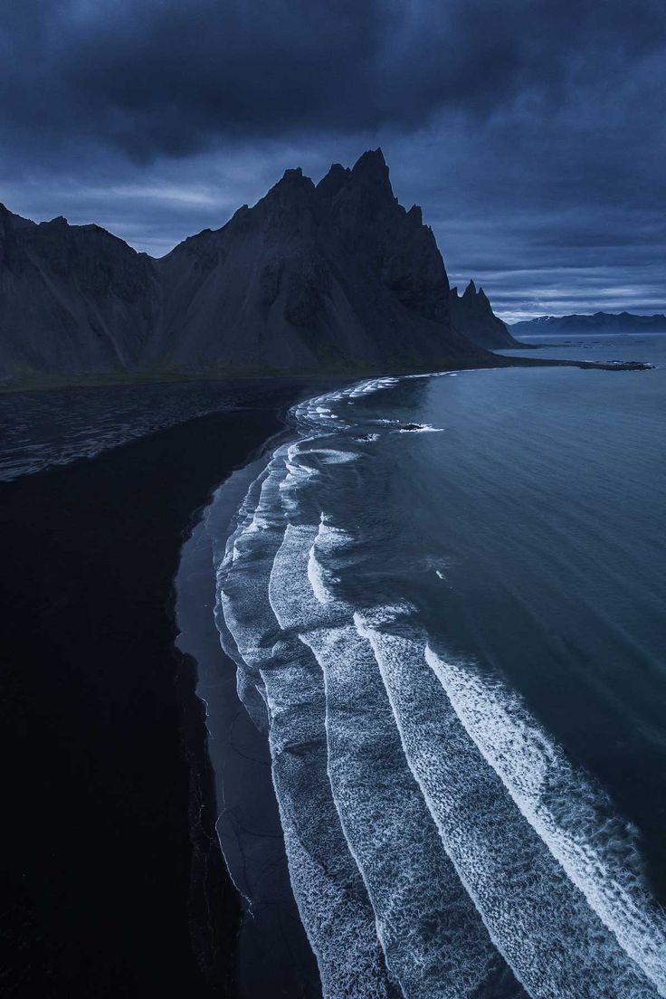 an ocean beach with waves coming in to the shore and mountains in the background at night