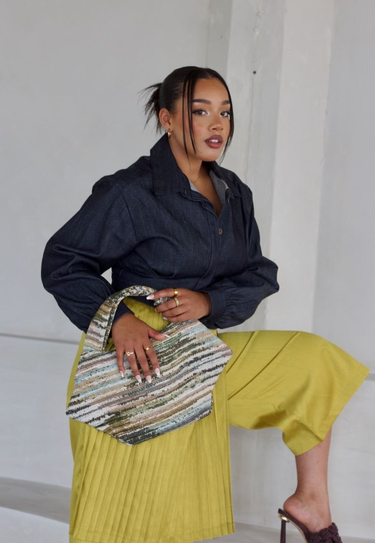 a woman sitting on top of a chair wearing a yellow pleated skirt and black shirt