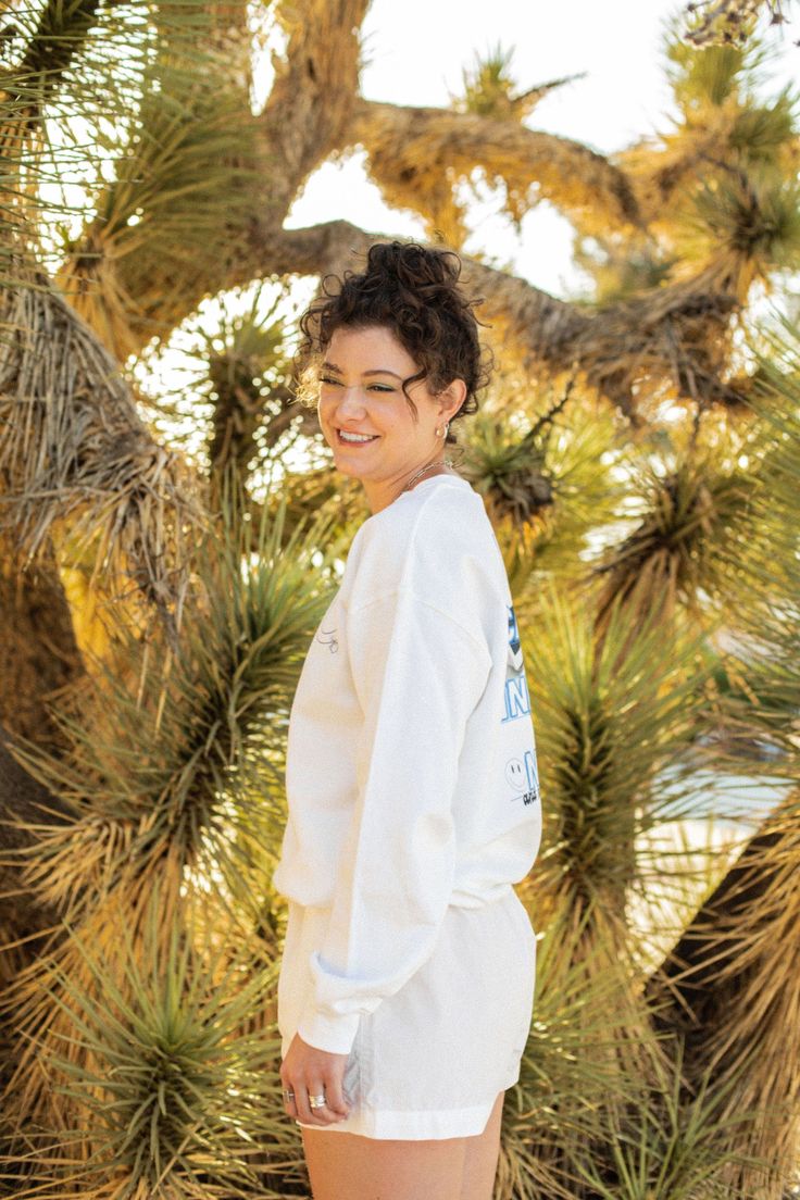 a woman standing in front of a tree wearing white shorts and a long sleeved shirt