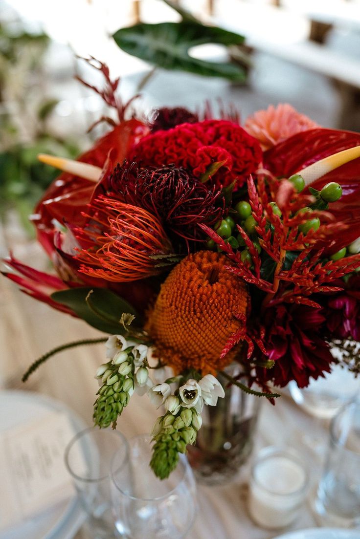 a vase filled with lots of red flowers on top of a table next to glasses