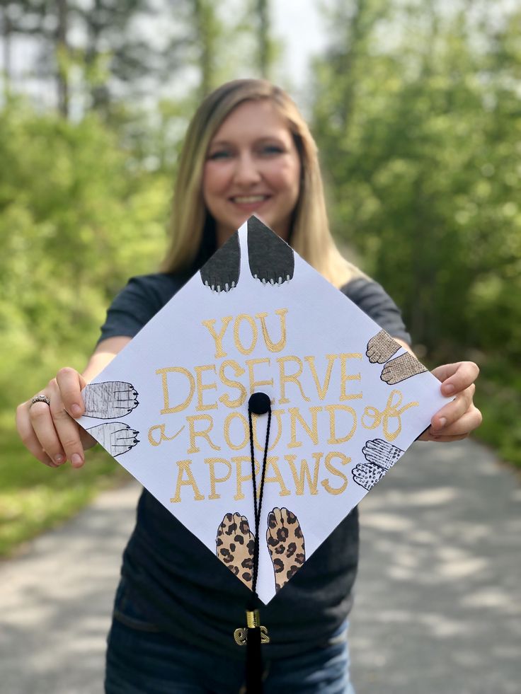 a woman holding up a graduation cap that says you deserving around apaws