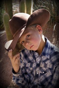 a young boy wearing a cowboy hat next to a cactus