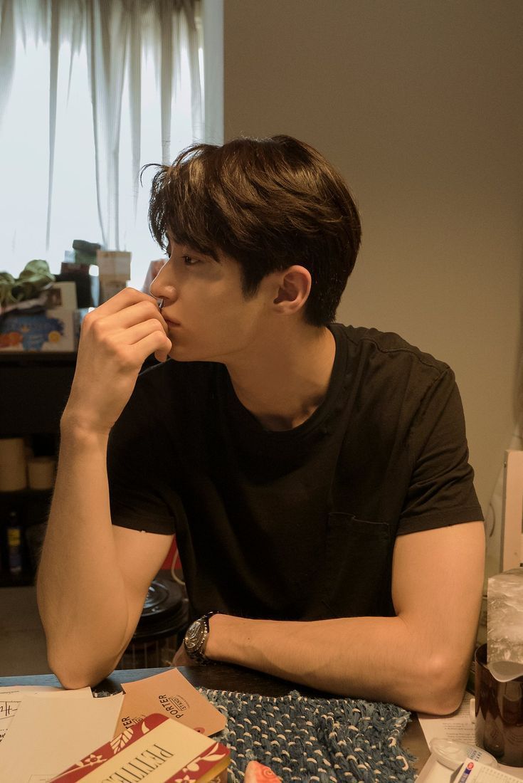 a young man sitting at a table with food in front of him and eating something out of his mouth