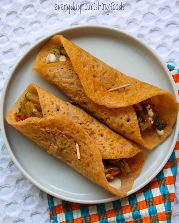 two tortillas on a white plate sitting on a checkered table cloth next to an orange and blue napkin