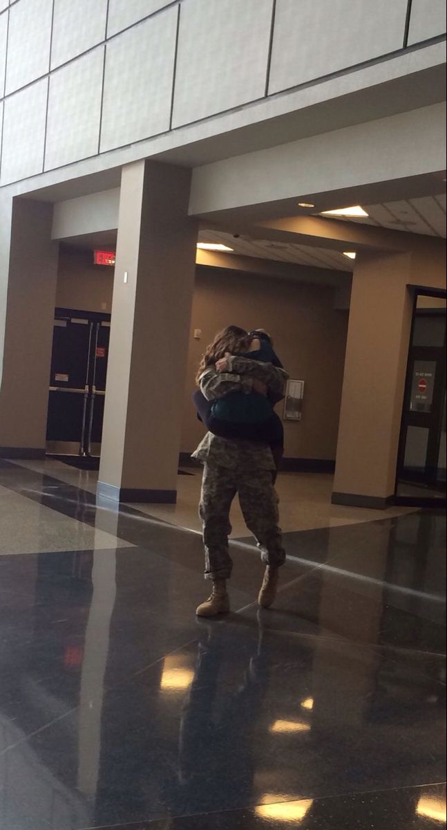 a man in camouflage carrying a backpack through an airport terminal lobby with his back to the camera