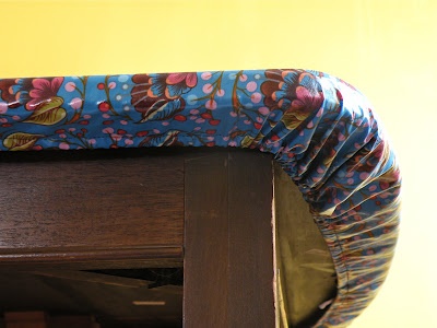 a close up of a clock on a wooden table with a cloth covering the top