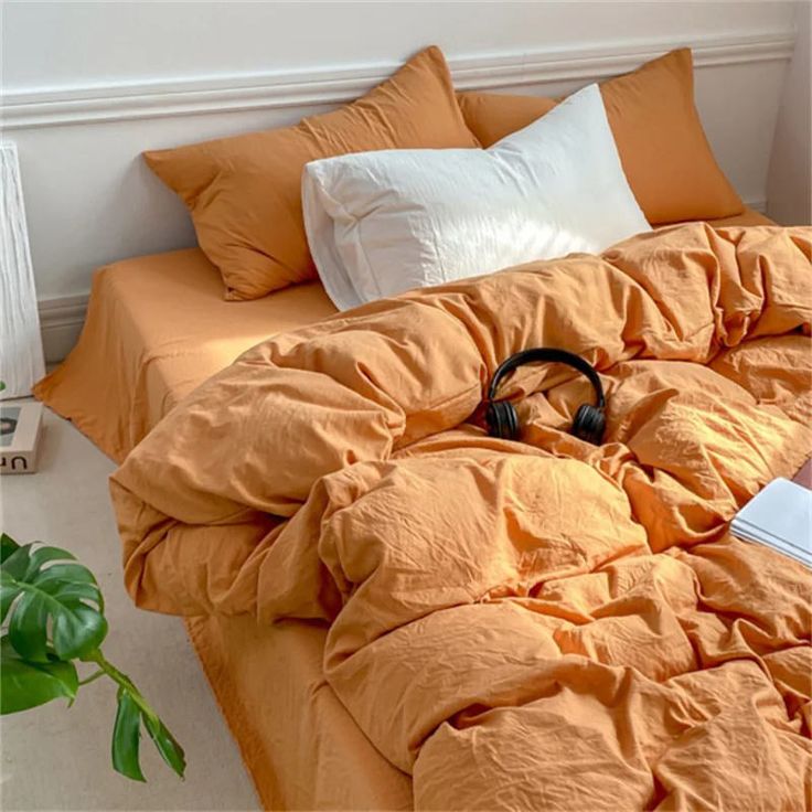 an orange comforter on a bed with headphones and a plant in the corner