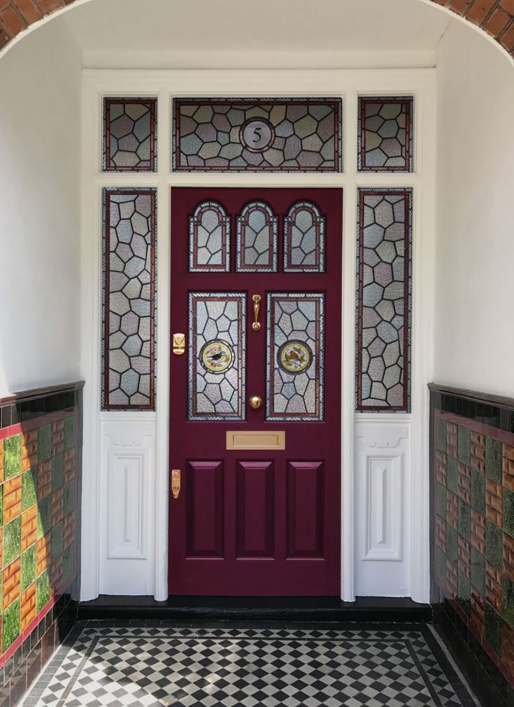 a red door with stained glass on the top and bottom panel is flanked by black and white checkered flooring