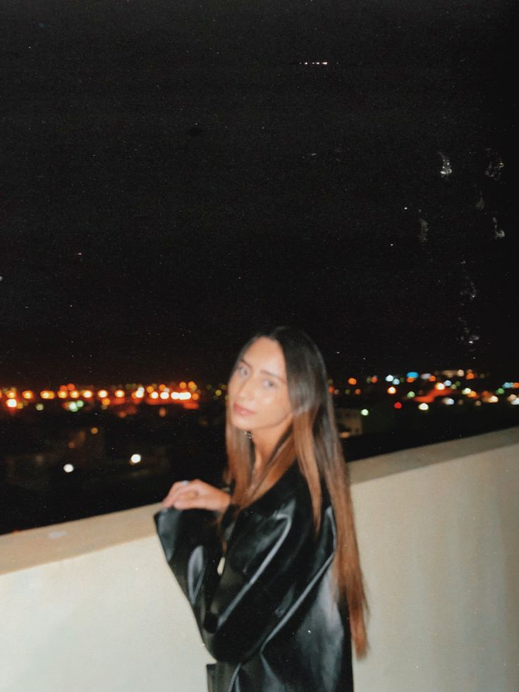 a woman standing on top of a balcony next to a wall with lights in the background