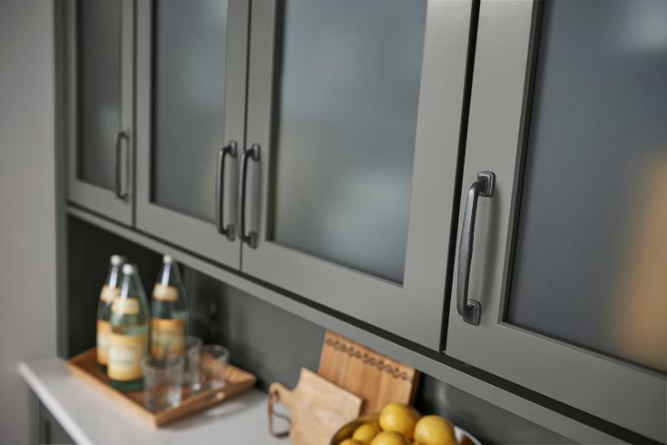 a kitchen with gray cabinets and fruit on the counter top in front of it is a wooden cutting board