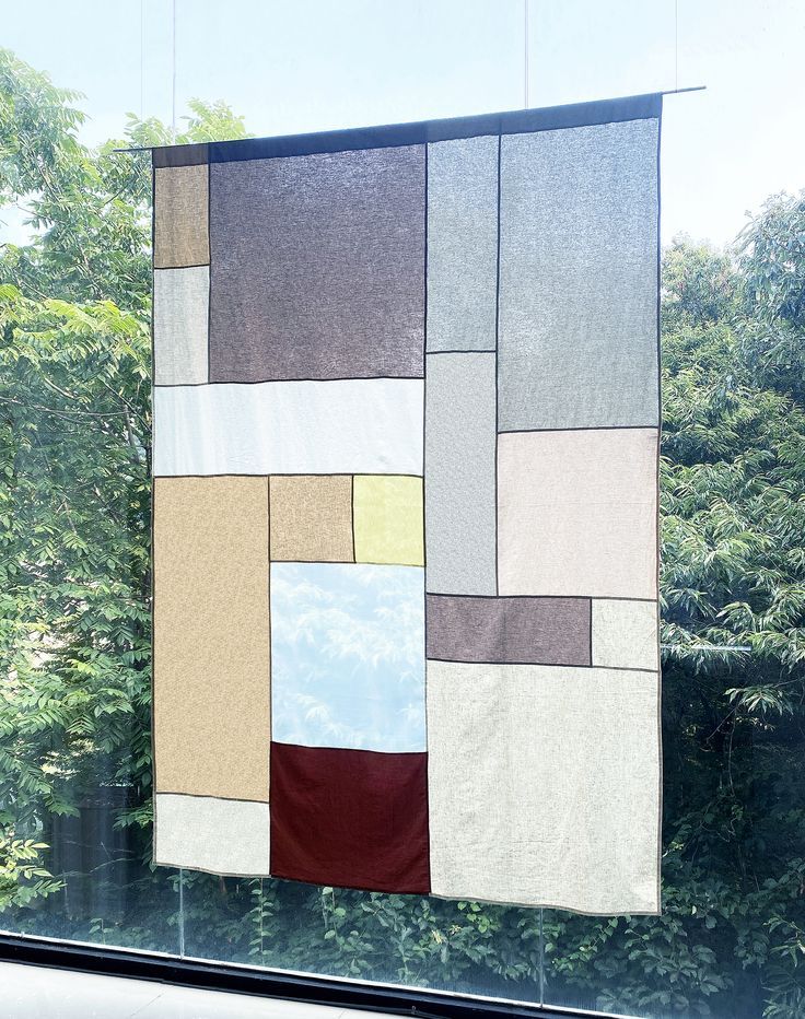 a patchwork quilt hanging on a window sill in front of some trees and bushes