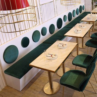 the tables are lined up against the wall with green velvet chairs and plates on them