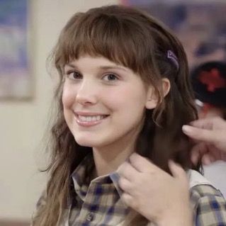 a girl is smiling and getting her hair styled by another person in the background,