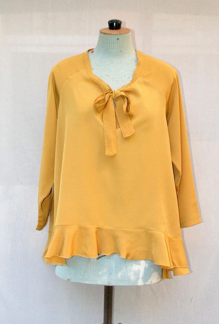 The  blouse is made of mustard yellow polyester crepe fabric. The shape blouses is wide and asymmetric (shorter in the front) and has a large ruffle on the blouse edge. You can tie the neckline or leave it open. Blouse length: Back: 70cm - Front: 50 cm Size: Fr  One size fit (38 to 42) Composition: 100% Polyester Care of clothing: Wash 30oC - Cool iron - Dry cleaning https://www.etsy.com/fr/shop/VLbasics?ref=seller-platform-mcnav Flowy Yellow Blouse For Fall, Chic Mustard Blouse For Fall, Yellow Ruffled Long Sleeve Blouse, Chic Tie Neck Flowy Blouse, Yellow Long Sleeve Blouse With Ruffles, Chic Mustard Top For Brunch, Chic Yellow Blouse, Yellow V-neck Ruffle Blouse, Flowy Yellow Blouse For Brunch