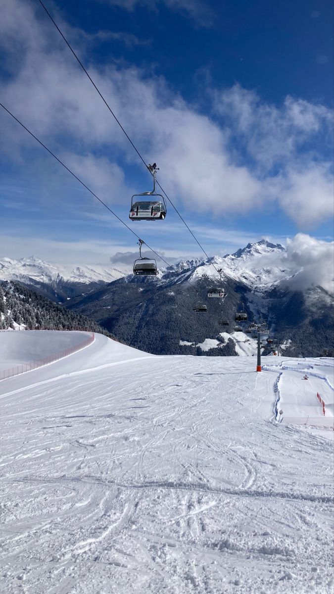 the ski lift is above the snow covered mountain range, with skiers on it