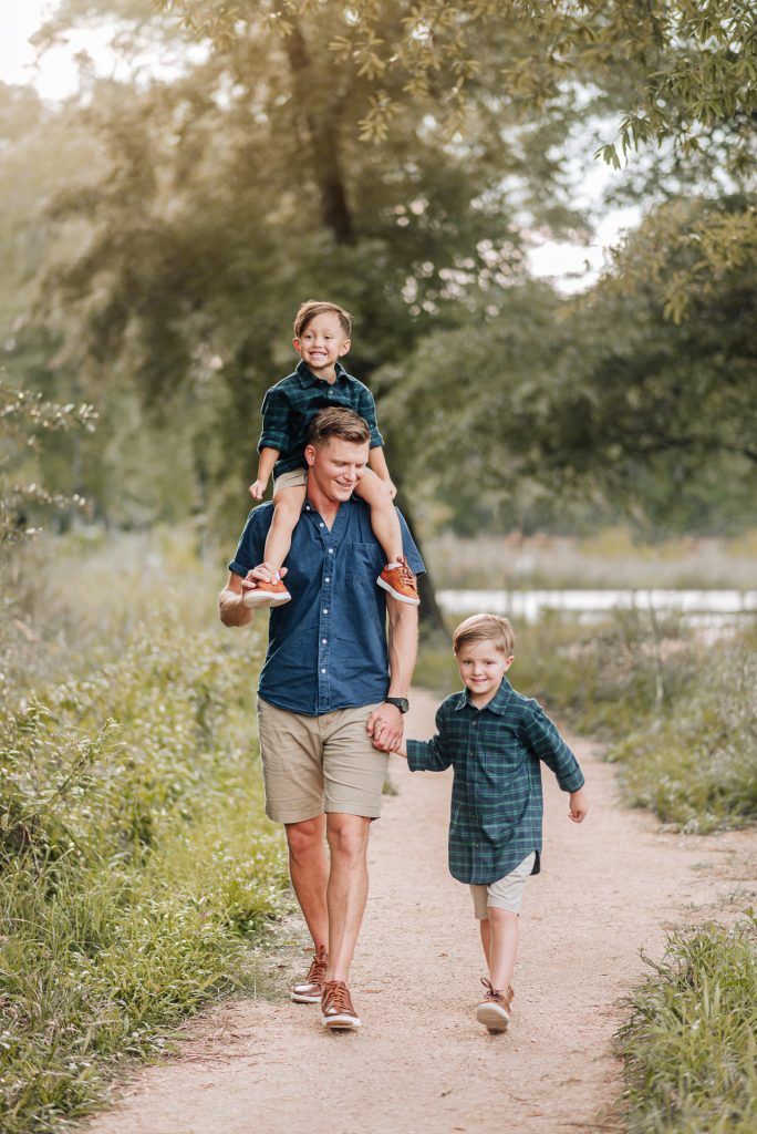 a man carrying a young boy on his shoulders while walking down a path