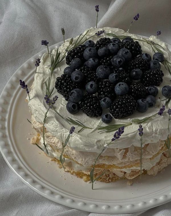 a white plate topped with a cake covered in blueberries and lavender sprigs