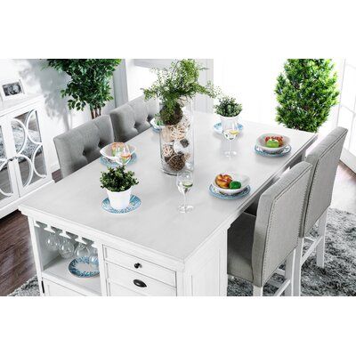 a dining room table with chairs and plates on it, surrounded by potted plants