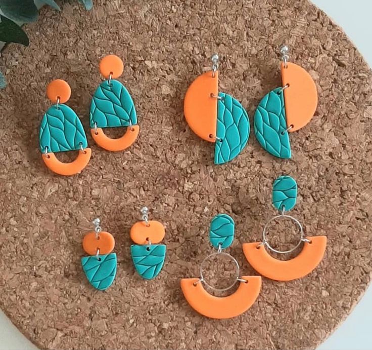 six pairs of orange and turquoise earrings on a cork board next to a potted plant