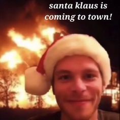 a young man wearing a santa hat in front of a large fire that is raging