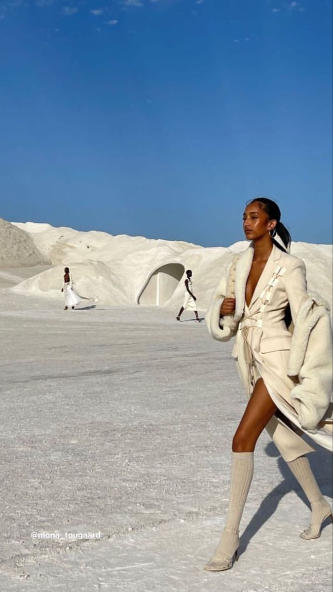 a woman is walking in the snow with her legs spread out and she has long white coat over her shoulders