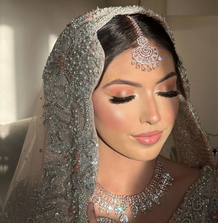 a woman wearing a bridal veil and headpiece with jewels on her forehead is looking at the camera