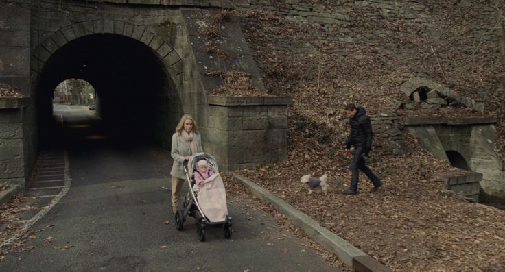 a woman pushing a stroller in front of a tunnel with two people walking by