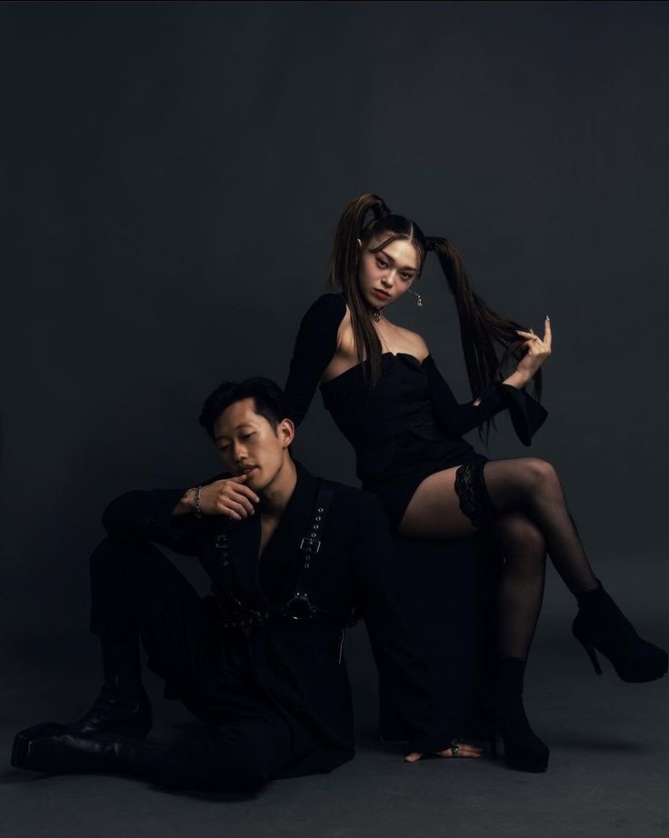 a man and woman posing for a photo in black outfits with one holding her hair