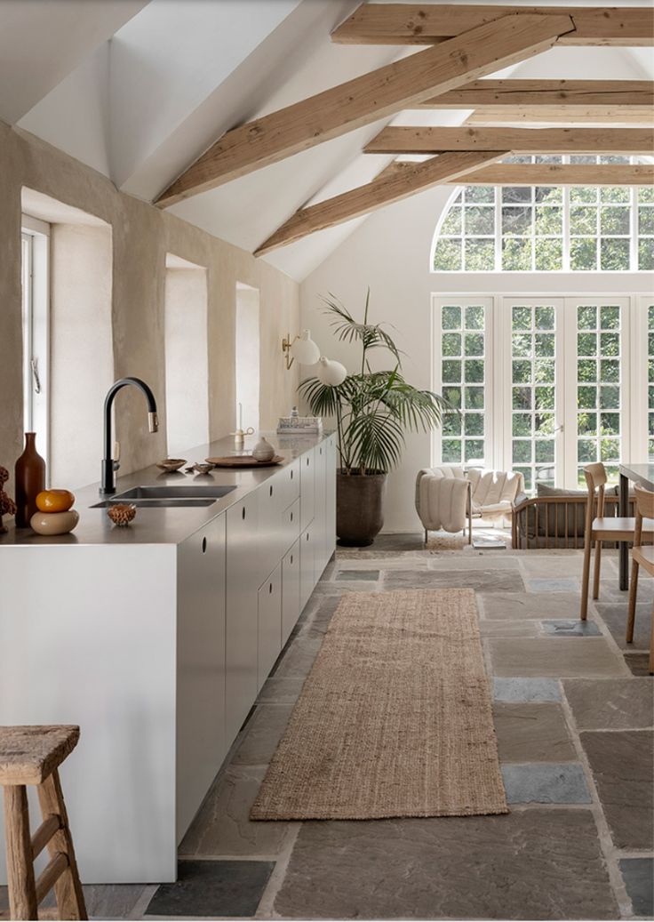 an open kitchen and dining area with wood beams on the ceiling, white walls, and large windows