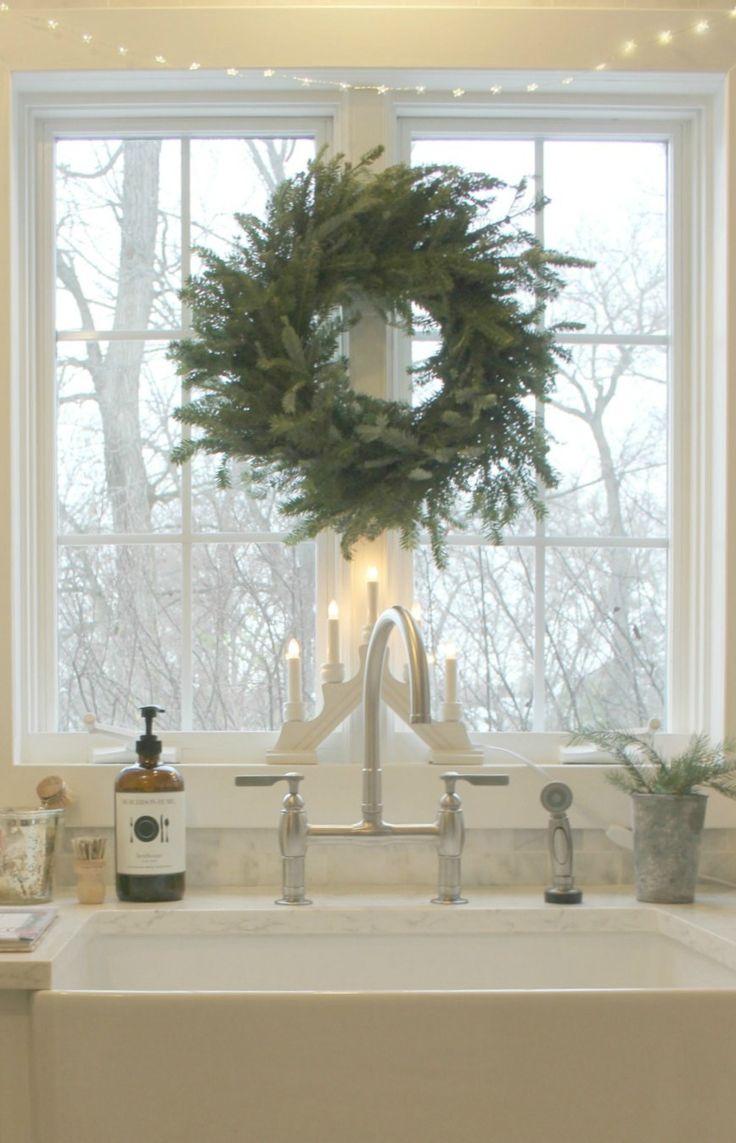 a white sink sitting under a window next to a wreath on top of a faucet