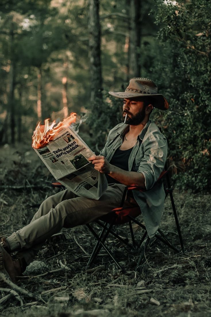 a man sitting in a chair with a newspaper on his lap while holding a fire