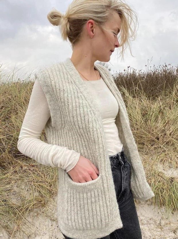 a woman standing on top of a sandy beach next to tall grass and sand dunes