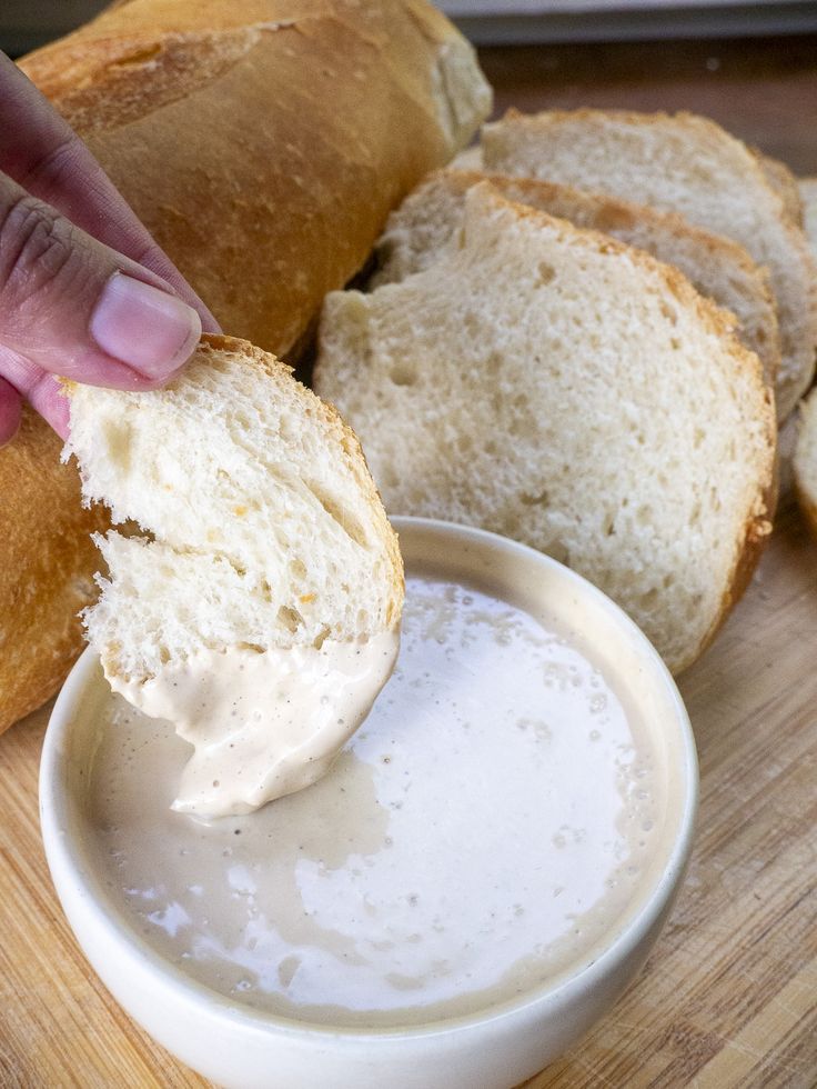 a person dipping something into a bowl with bread in the background